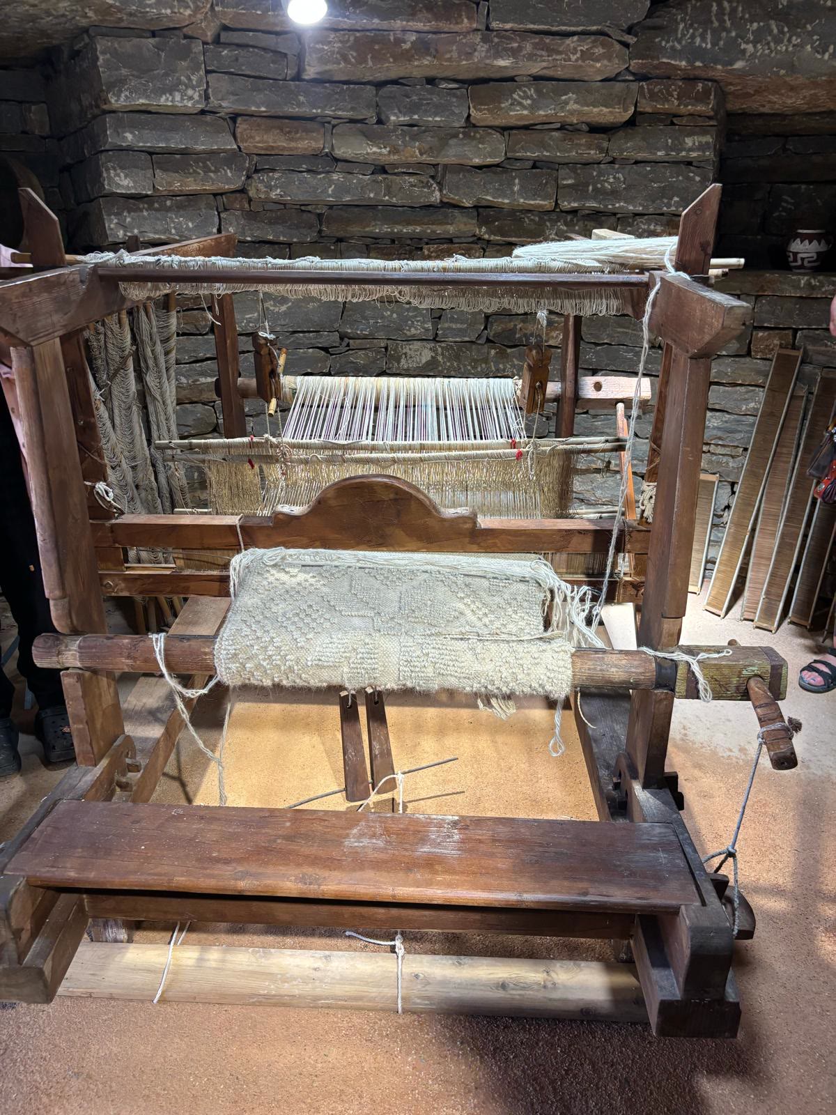 A traditional wooden loom with undyed wool in a stone-walled room.