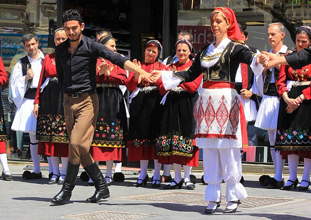 Dancers in traditional Cretan dress, hands joined, moving together in a circle dance.
