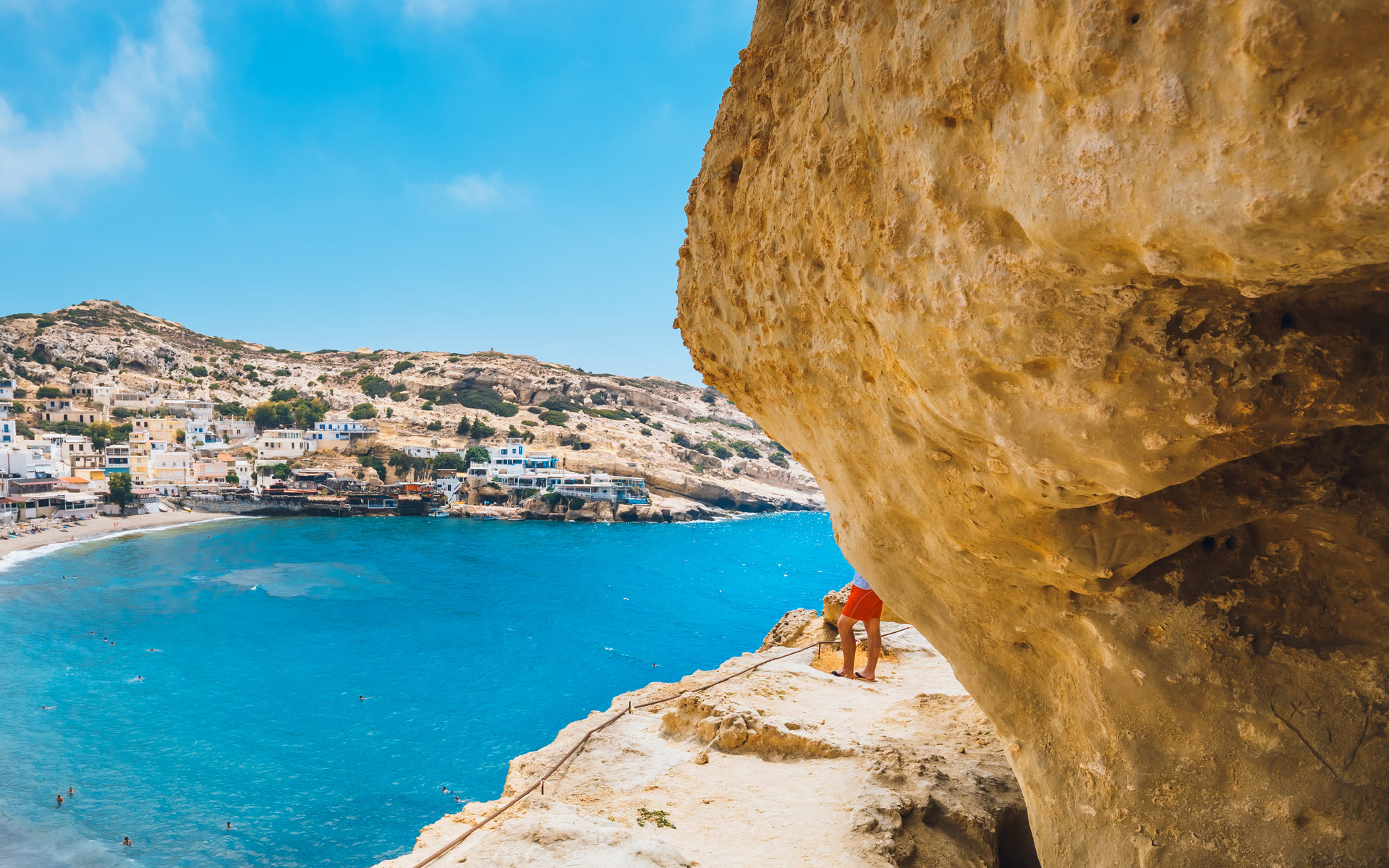 From the carved sandstone caves of Matala, on the south coast of Crete, the view opens over a deep blue bay and a whitewashed village.